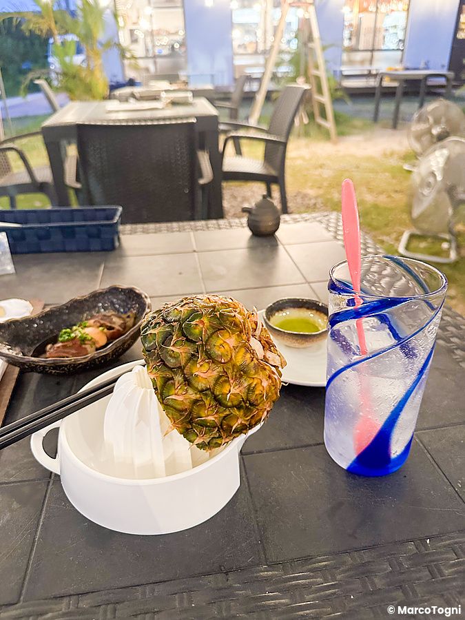 Drink all'ananas fresco da spremere su un tavolo di Izakaya Ichitaka a Iriomote con piatti di cucina locale.