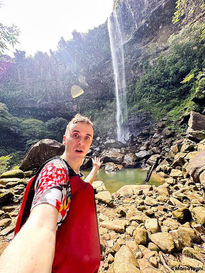 Marco Togni davanti alla cascata di Pinaisara a Okinawa, circondato dalla natura.