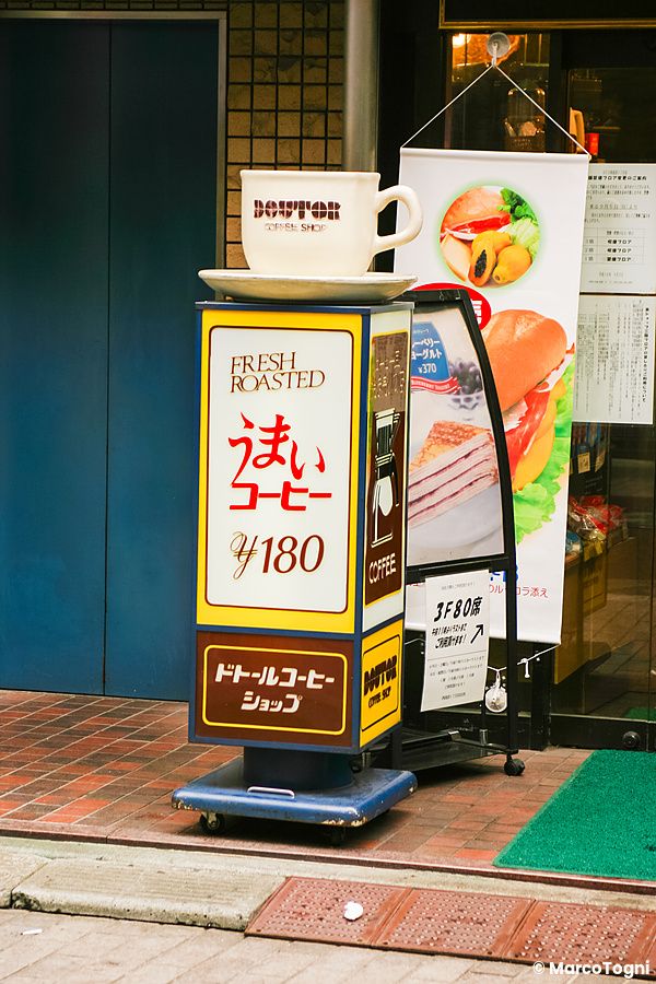Un cartello informativo e pubblicitario del Doutor Coffee Shop, Tokyo, posizionato su un marciapiede davanti all'entrata.