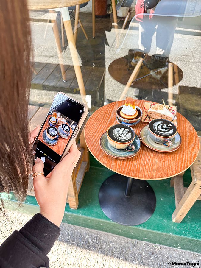 Una persona fotografa caffè e dolci su un tavolino rotondo all'esterno del Liwei Coffee Stand, Tokyo.