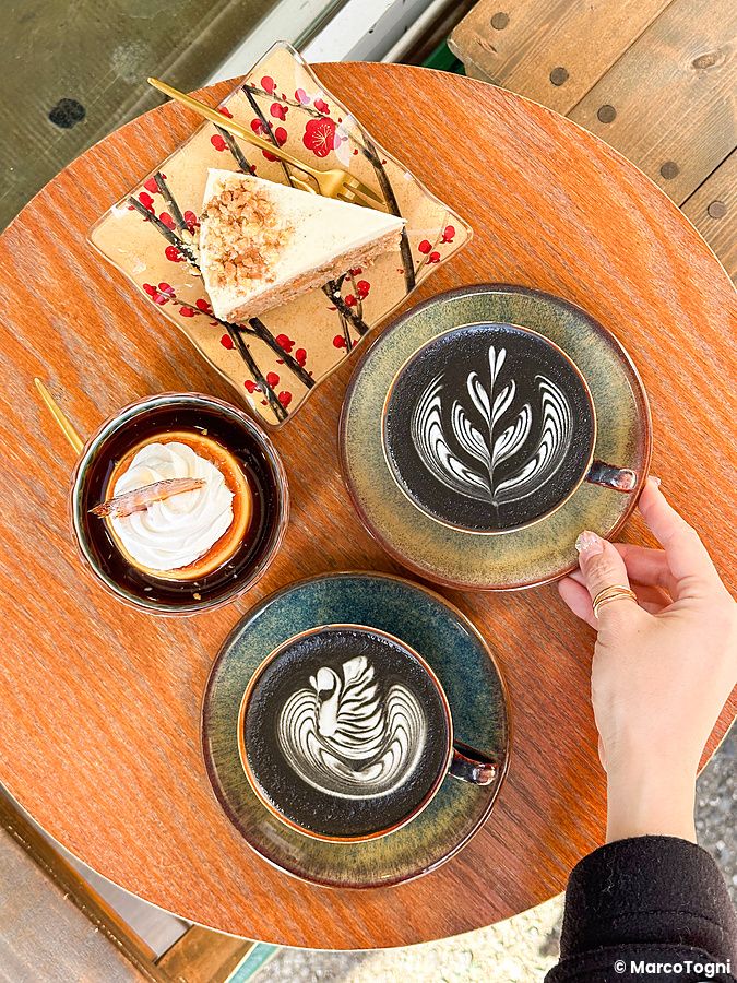 Due tazze di caffè con latte art, una fetta di torta e un dolce al cucchiaio su un tavolo da Liwei Coffee Stand, Tokyo.