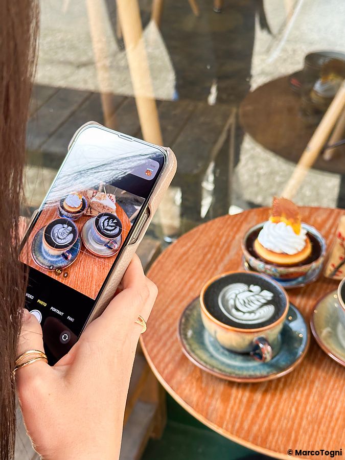 Una persona fotografa con lo smartphone tazze di caffè e un dolce presso il Liwei Coffee Stand, Tokyo.