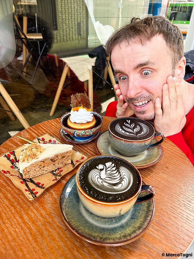 Marco Togni sorride accanto a caffè e dolci su un tavolo circolare presso il Liwei Coffee Stand, Tokyo.