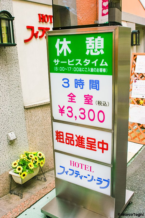 Un cartello luminoso informativo per un love hotel a Shibuya che elenca tariffe e orari di servizio.