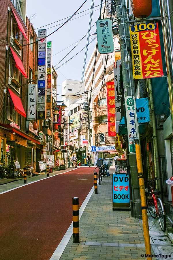 Una strada di Shibuya a Tokyo fiancheggiata da numerosi cartelli pubblicitari verticali e negozi.