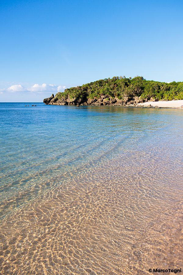La spiaggia Mimikiri sull'isola di Iriomote a Okinawa mostra acque limpide che bagnano una costa con vegetazione fitta.