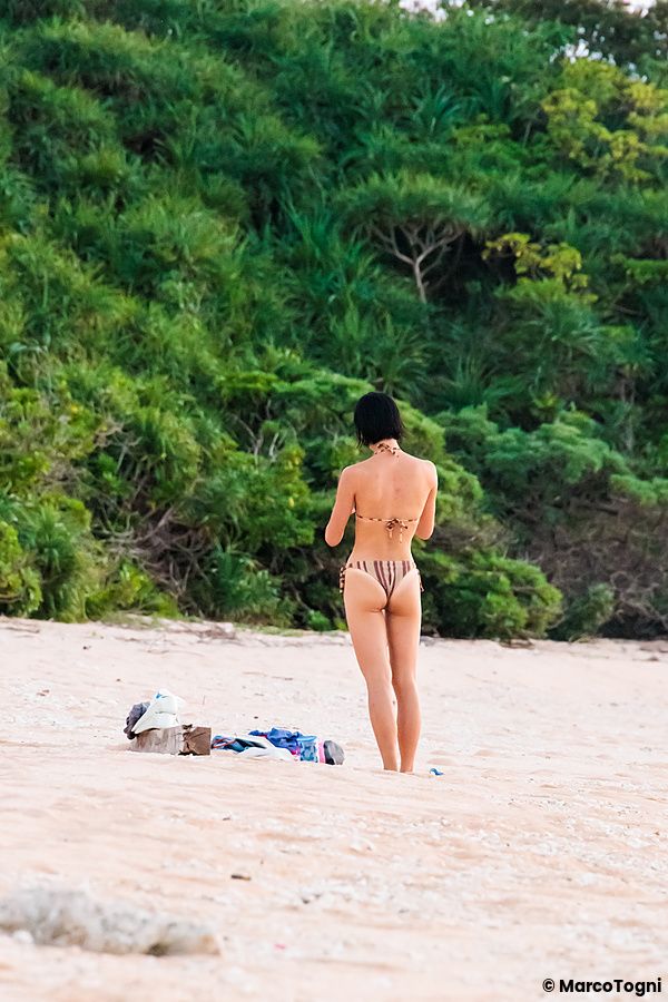 Ragazza su una spiaggia deserta a Okinawa con vegetazione verde alle spalle.