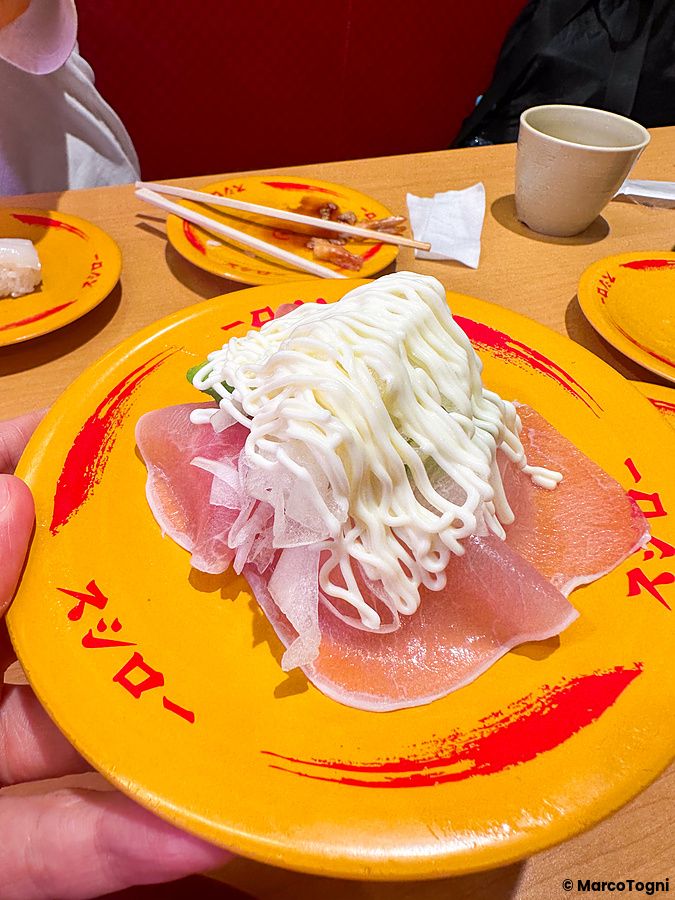 Un piatto giallo con il logo del Ristorante Sushiro che contiene sushi guarnito con prosciutto e maionese.