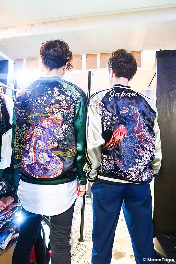 Due persone a Tokyo indossano giacche bomber in stile souvenir con ricami colorati visti di spalle in un negozio.