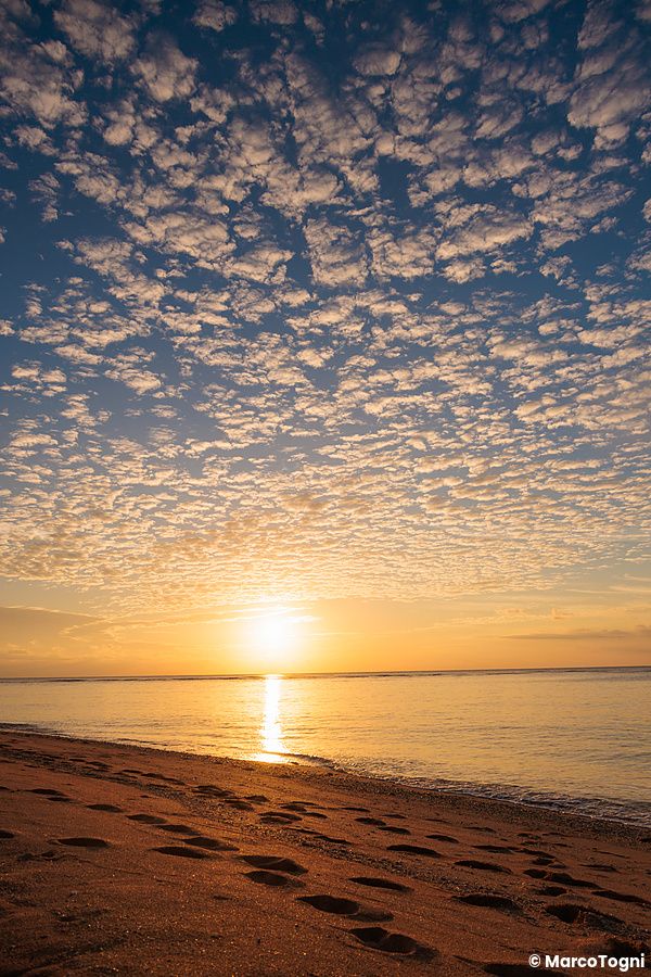 Tramonto dorato sulla spiaggia Mimikiri, sull'isola di Iriomote a Okinawa, con impronte sulla sabbia in primo piano.