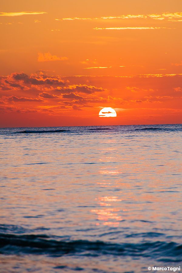 tramonto sulla spiaggia Mimikiri con cielo arancione e mare calmo.