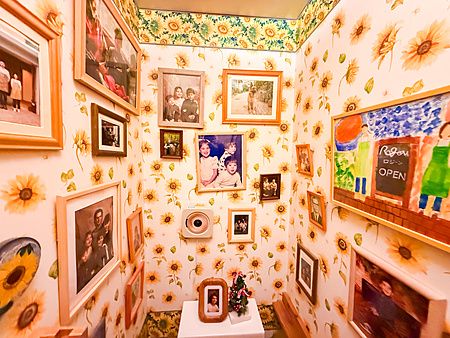 Pareti decorate con carta da parati a girasoli e numerose cornici di fotografie nel bagno del caffè RoJean a Tokyo.