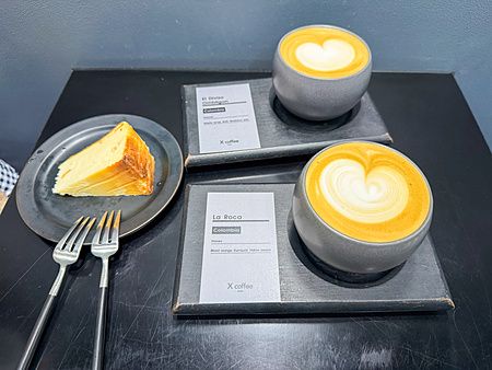 Due tazze di caffè con latte art e una fetta di dolce su un tavolo nero presso X coffee a Ginza, Tokyo.