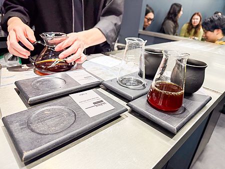 Bancone in acciaio di X coffee a Ginza con vassoi in legno, caraffe di vetro e una persona che serve il caffè.