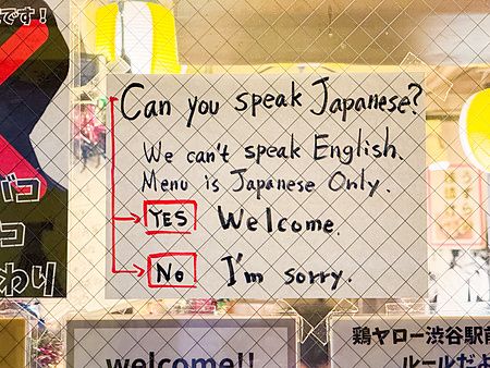 Un cartello scritto a mano in inglese su una vetrata in Giappone che indica le limitazioni linguistiche del locale.