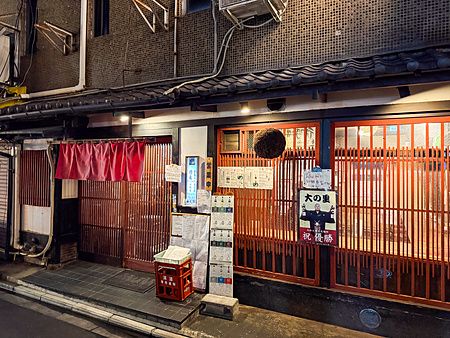 L'esterno di Gion Yuki a Kyoto presenta una facciata in legno scuro con infissi a listelli rossi e insegne informative.