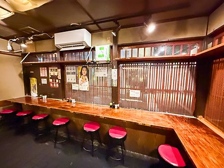 Interno a Gion Yuki, un izakaya a Kyoto con bancone in legno e sgabelli rossi allineati lungo la parete decorata.