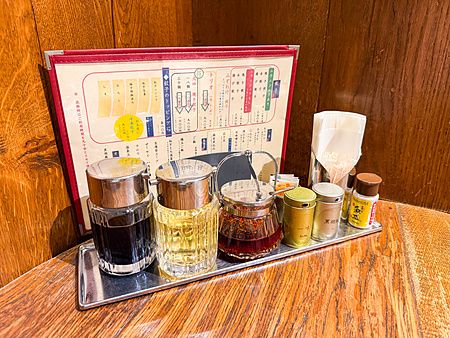 Set di condimenti in contenitori di vetro e metallo su un tavolo di legno presso il ristorante Gyoza no Fukuho a Tokyo.
