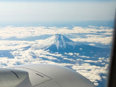 Vista aerea del Monte Fuji innevato che emerge sopra una distesa di nuvole visto dal finestrino di un aereo.