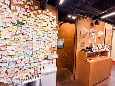 Una parete dell'interno a Café Giang a Yokohama coperta di post-it colorati vicino a un lavabo e una scala.