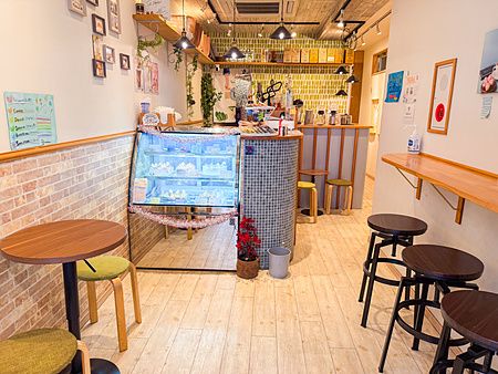 Interno a Shochikuen, un locale ad Asakusa con vetrina di dolci, tavoli in legno e sgabelli su pavimento chiaro.
