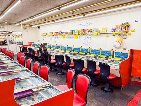 Interno della sala giochi Smartball New Star a Osaka con file di macchine da gioco vintage e sedie rosse.