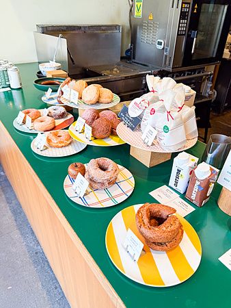 Vari donut vegani disposti su piatti colorati sul bancone verde del negozio Sunday Vegan a Kichijoji.