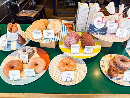 Vetrina di donut vegani esposti su piatti colorati con cartellini dei prezzi presso il negozio Sunday Vegan a Kichijoji.