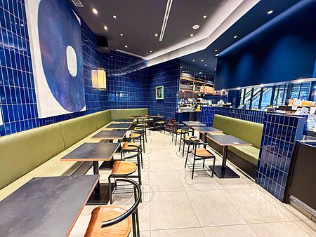 Interno della sede di The City Bakery a Shibuya con piastrelle blu, divanetti verdi e tavoli neri disposti in fila.