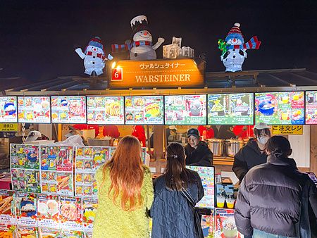 Persone in fila davanti a una bancarella illuminata al Tokyo Christmas Market presso il Meiji Jingu Gaien.