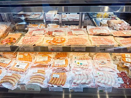 Una vetrina refrigerata del ristorante König a Kichijoji piena di pacchetti di wurstel e salumi etichettati.