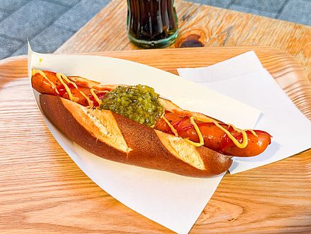 Un hot dog con pane tipo pretzel, senape, ketchup e cetriolini servito su un vassoio di legno da König a Kichhijoji.
