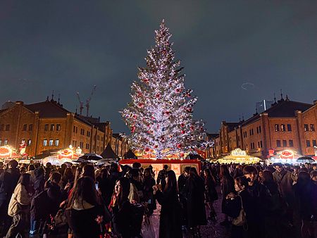 Un grande albero di Natale illuminato al centro del Yokohama Red Brick Christmas Market circondato da molte persone.
