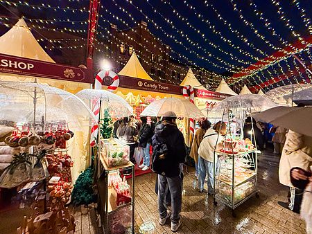 Persone con ombrelli trasparenti visitano le bancarelle illuminate del Yokohama Red Brick Christmas Market di sera.