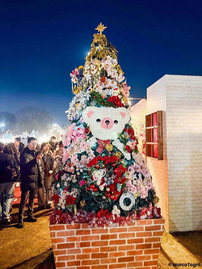 Un albero di Natale decorato con peluche a forma di orso al Tokyo Christmas Market, con persone intorno.