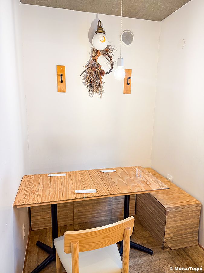 Un tavolo in legno con sedia e panca all'interno a Chaka, un locale nel quartiere di Kita-Senju a Tokyo.