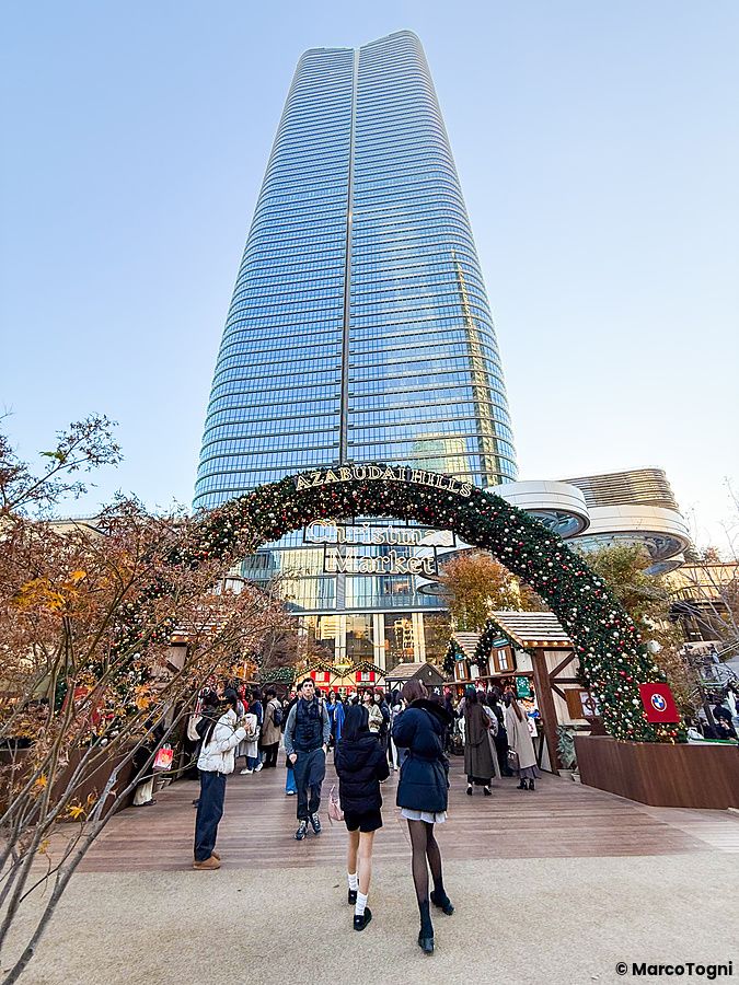 Un arco decorato all'ingresso del mercatino di Natale di Azabudai Hills con il grattacielo Mori JP Tower sullo sfondo.