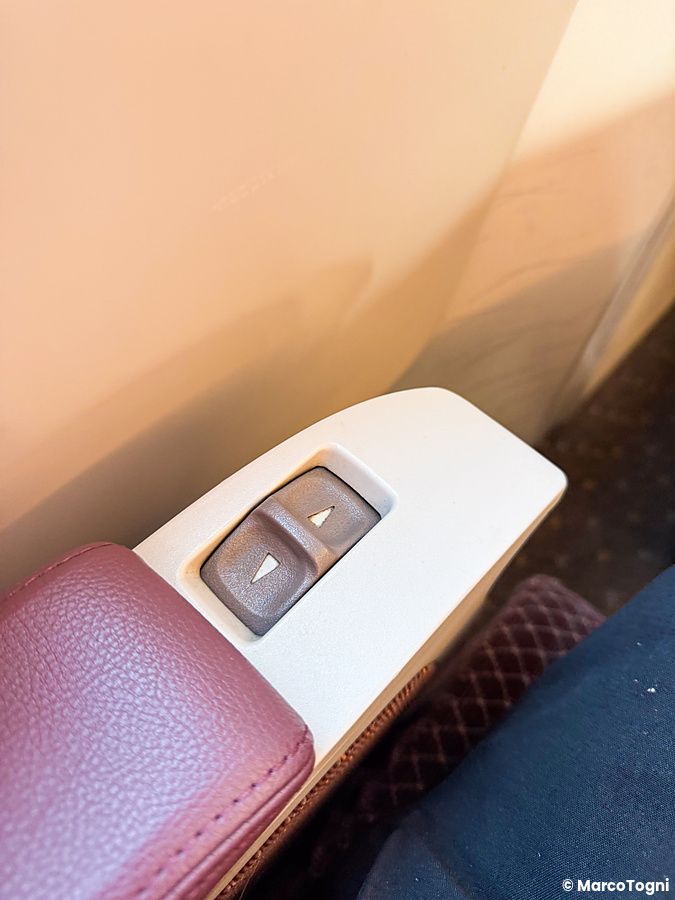 Dettaglio di due pulsanti grigi integrati nel bracciolo bordeaux per regolare il sedile sulla green car sul treno shinkansen.