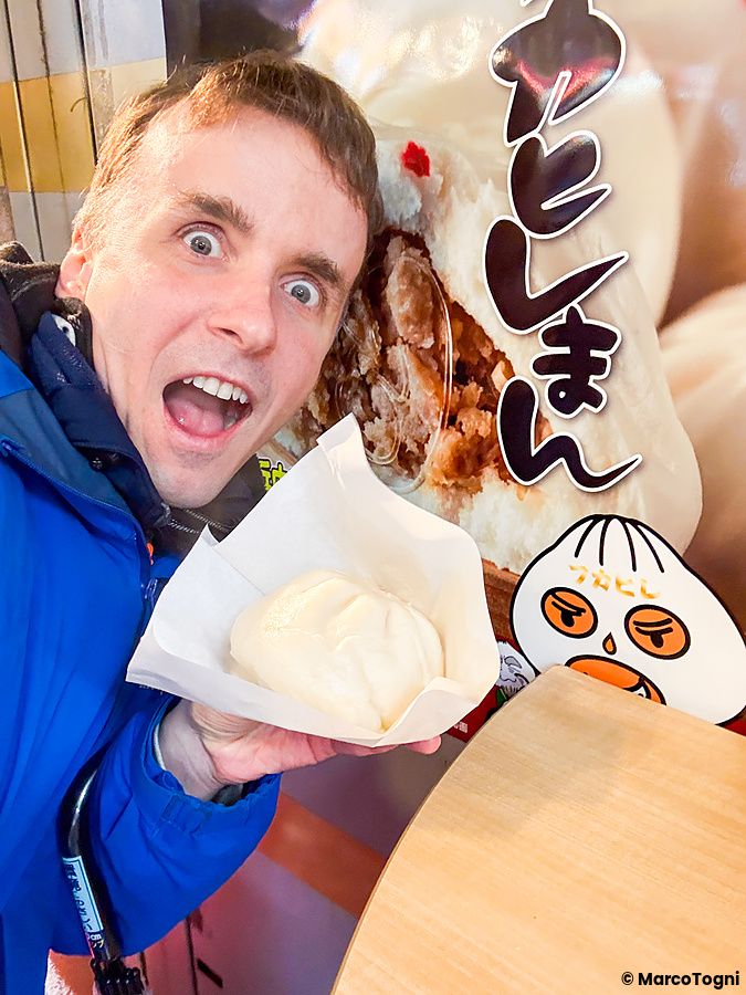 Marco Togni tiene un butaman a Koseiwa davanti a una pubblicità dello stesso prodotto presso il negozio Koseiwa.