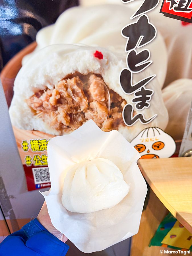 Una mano tiene un butaman a Koseiwa in Chinatown a Yokohama davanti a un cartellone pubblicitario del negozio.