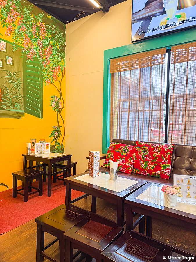 Interno a Café Giang a Yokohama con tavoli in legno, sgabelli e un divano con cuscini rossi decorati.