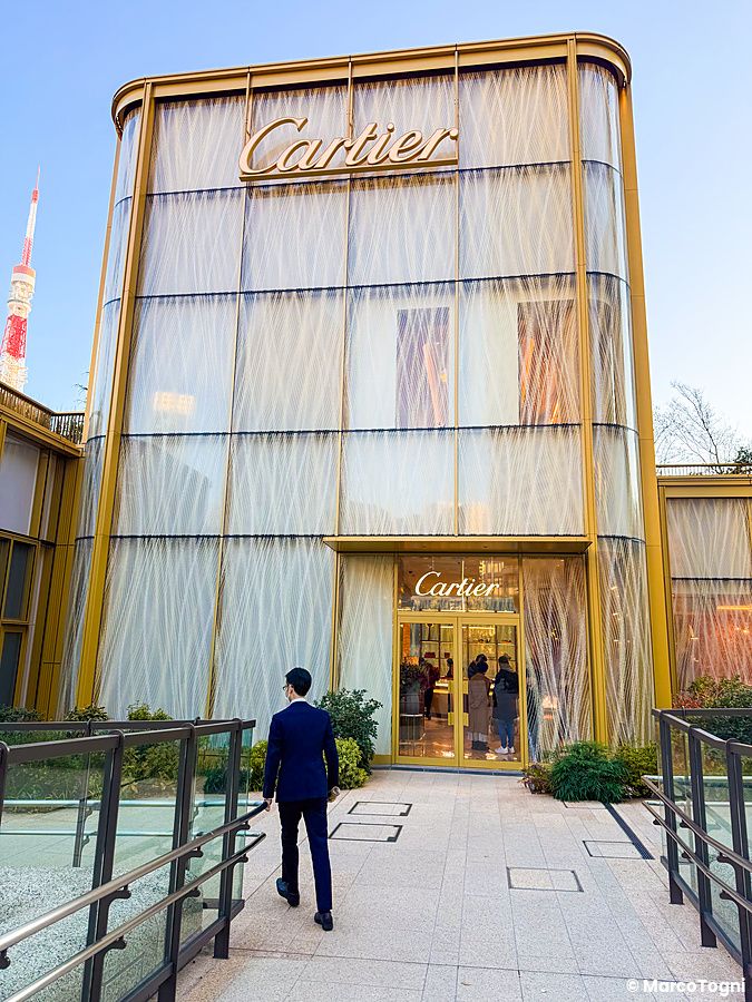 Un uomo in completo cammina verso l'ingresso dorato del negozio Cartier nel complesso di Azabudai Hills a Tokyo.