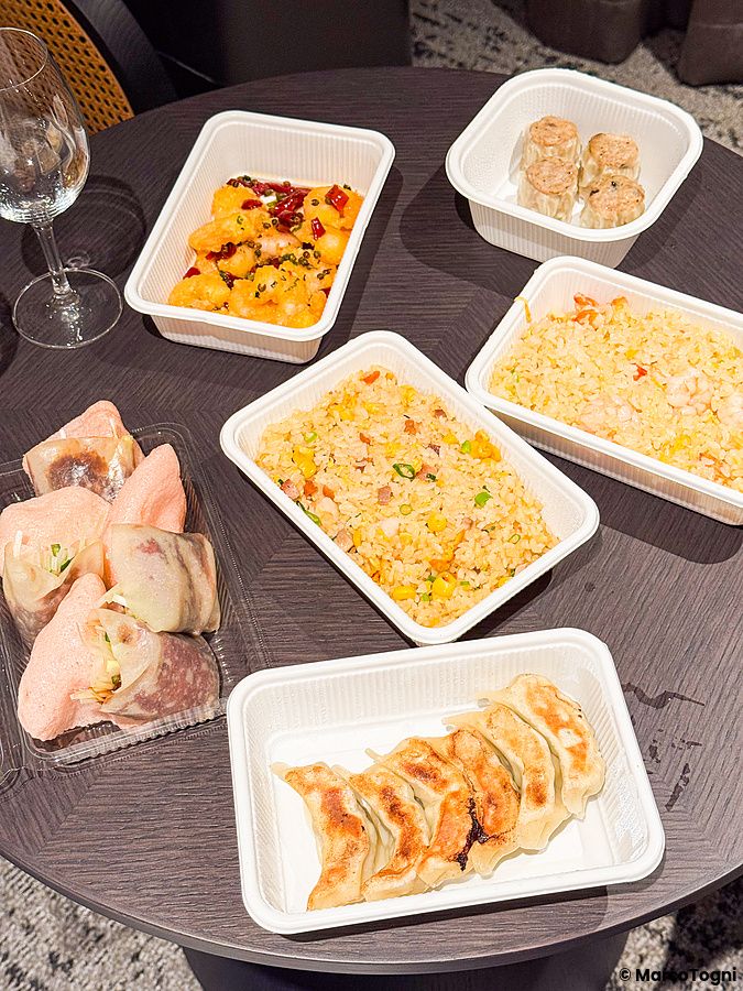 Diverse porzioni di cibo cinese d'asporto a Wangfujing disposte in contenitori di plastica su un tavolo circolare.