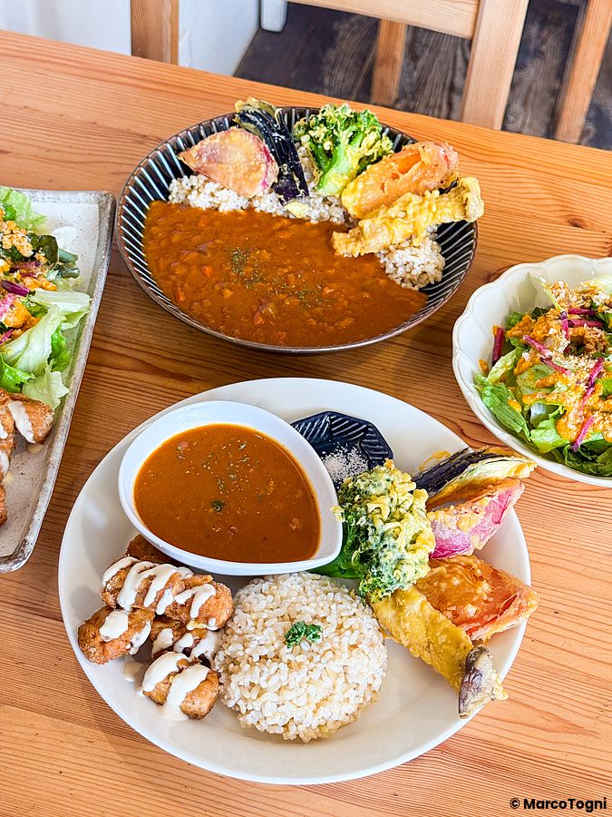 Piatti con curry, insalata, falafel e verdure in tempura serviti su un tavolo in legno presso Marugoto ad Asakusa.