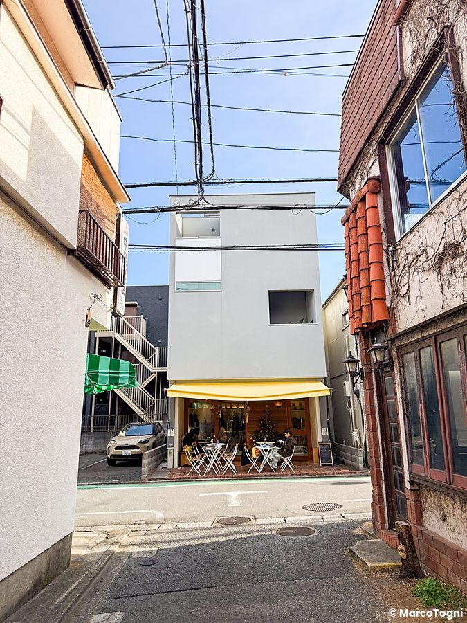 L'edificio a RoJean è un piccolo caffè a Tokyo con una tenda gialla, tavolini all'aperto e persone sedute.