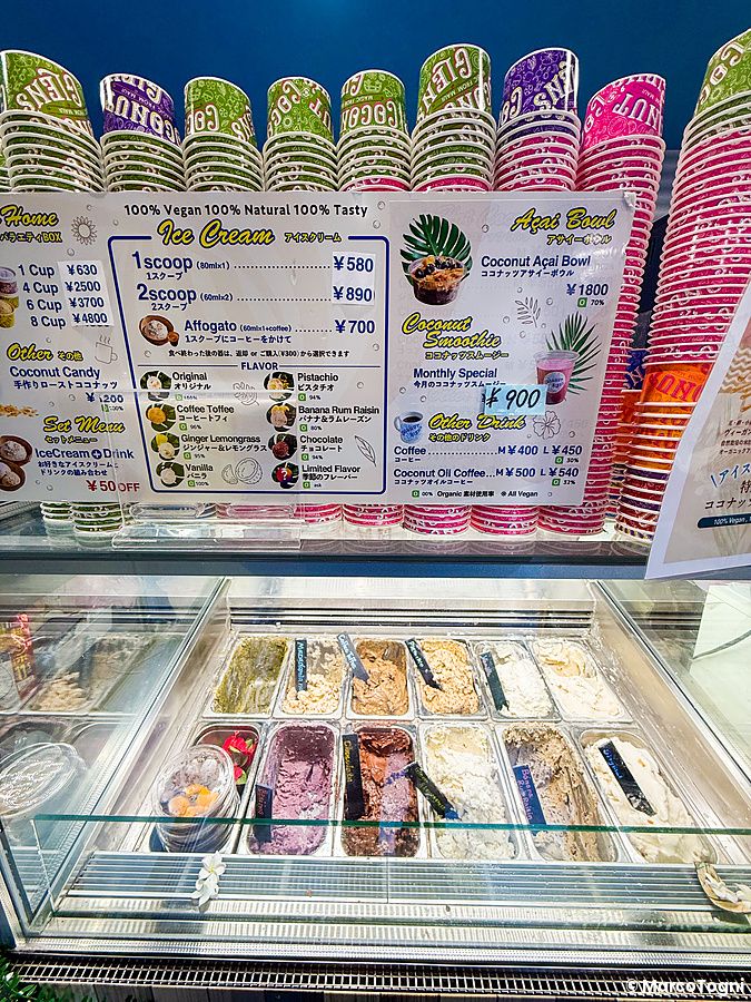 Il bancone refrigerato di Coconut Glens in Giappone con vaschette di gelato vegano e il menu esposto sopra.