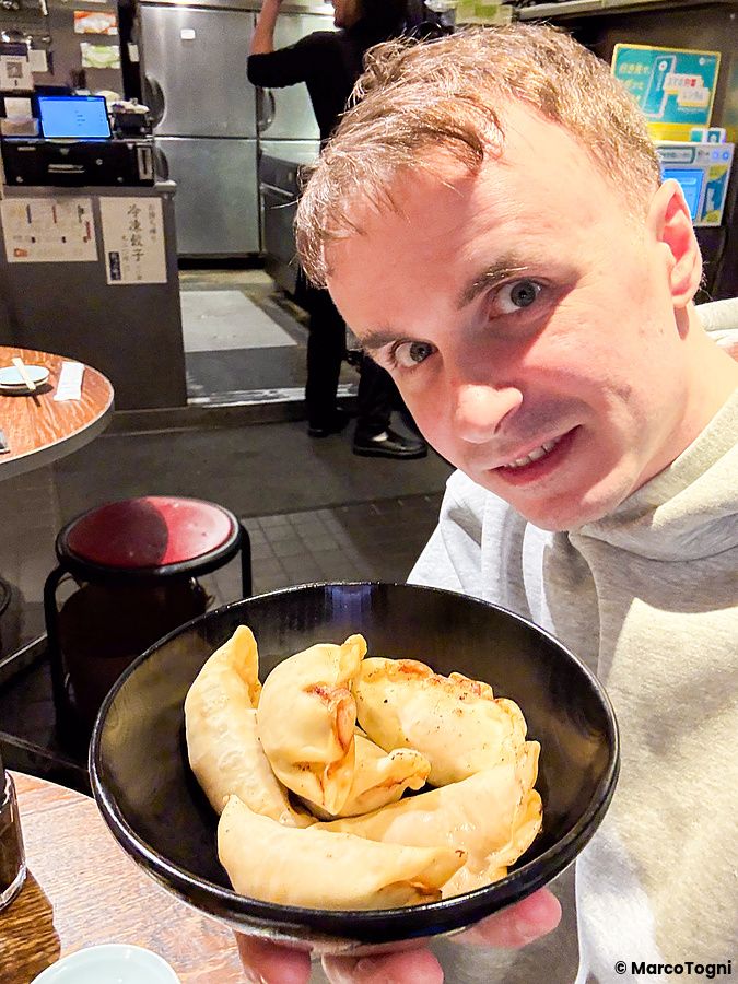 Marco Togni tiene in mano una ciotola di gyoza fritti a Gyoza no Fukuho all'interno del ristorante a Tokyo.