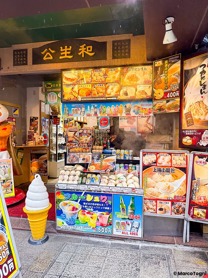 L'ingresso a Koseiwa nella Chinatown di Yokohama con un bancone ricco di menu, poster di cibo e un individuo al lavoro.