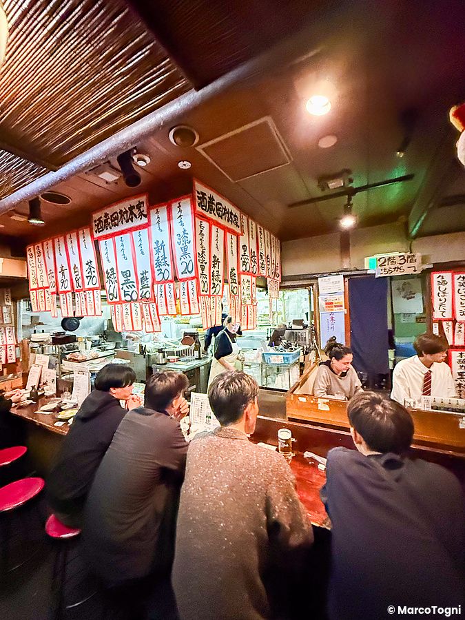 L'interno a Gion Yuki con persone sedute al bancone e numerosi cartelli menu appesi al soffitto in legno.