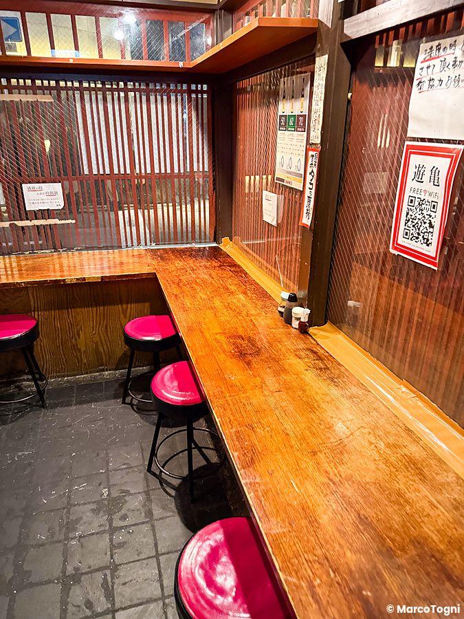Interno a Gion Yuki a Kyoto con bancone in legno e sgabelli rossi allineati lungo una parete con pannelli.